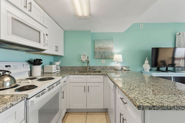 A kitchen with white cabinets, a granite countertop, a microwave, a stove, and a sink.