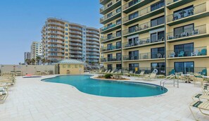 A pool area with lounge chairs and a small pool, surrounded by multi-story buildings with balconies. - Ocean View Suite w/ Pool, Hot Tub & Beach Access (Daytona Beach Shores)