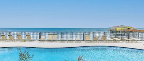 A pool area with lounge chairs and a view of the ocean.