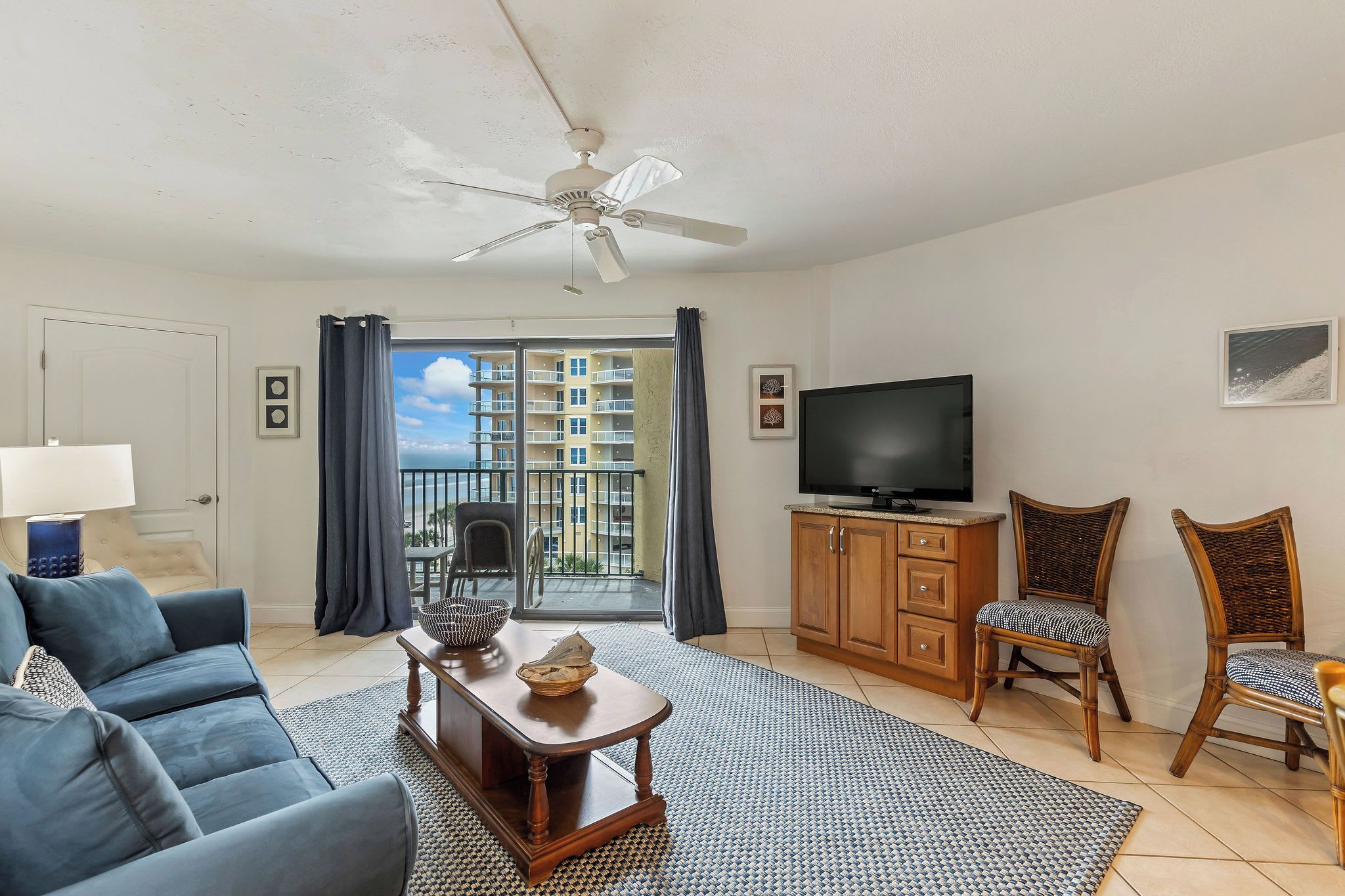 A living room with a sofa, a TV, a ceiling fan, and a view of a balcony.