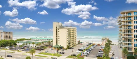 A beachfront hotel with multiple floors, a parking lot, and a view of the ocean.
