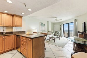 A spacious living area with a kitchen, dining table, and a balcony with a view. - Tropical Palms | Partial Ocean View, Pool, Hot Tub (Daytona Beach Shores)