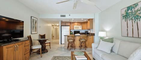A modern living room with a flat-screen TV, a sofa, a coffee table, and a dining area with a table and chairs.