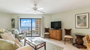 Un salon comprenant un canapé, des fauteuils, un téléviseur et un balcon avec vue sur l’océan.