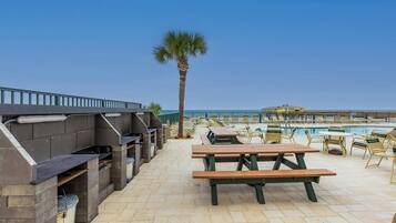 An outdoor patio with barbecue grills, picnic tables, and lounge chairs by a pool.