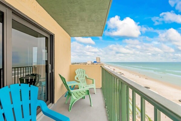 Un balcon avec vue sur la plage, une porte vitrée et deux chaises vertes.