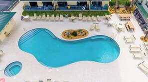 Une grande piscine de forme irrégulière, entourée de chaises longues et de tables, et une petite piscine circulaire située à proximité.
