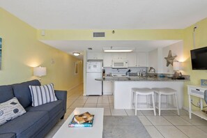 A compact living space with a kitchenette, a sofa, a coffee table, and a TV. - Breathtaking Views, Heated Pool & Beach Access! (Daytona Beach Shores)