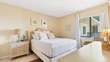 Quarto com cama, mesa de cabeceira, luminária e janela com cortinas.