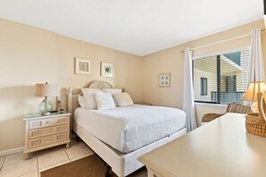 Quarto com cama, mesa de cabeceira, luminária e janela com cortinas.