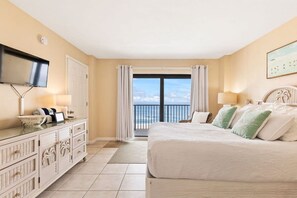 Quarto de hotel com uma cama grande, televisão presa na parede, cômoda e varanda com vista para o mar.