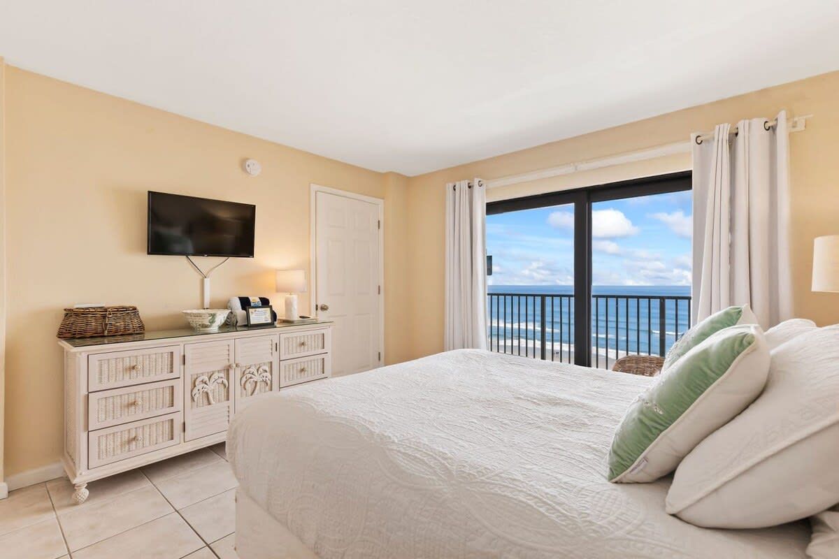 Quarto com uma cama grande, televisão na parede, cômoda e janela com cortinas.