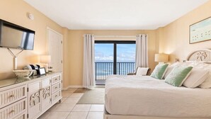 A hotel room with a large bed, a TV mounted on the wall, a dresser, and a balcony with a view of the sea. - Ocean Front Condo w/ Amazing Views, Pool & Hot Tub (Daytona Beach Shores)