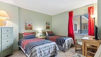 Quarto com duas camas, uma escrivaninha, uma cadeira e uma janela com cortinas.