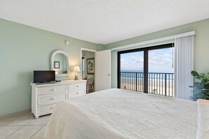 Un dormitorio con una cama grande, un aparador, un televisor y vista a la playa a través de una puerta abierta.