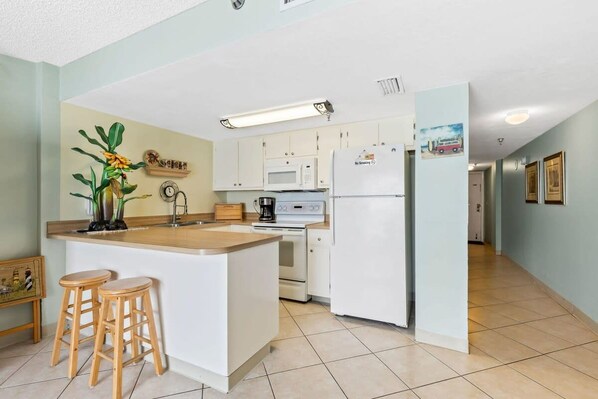 A compact kitchen with white cabinets, a microwave, a refrigerator, and a small island with stools.