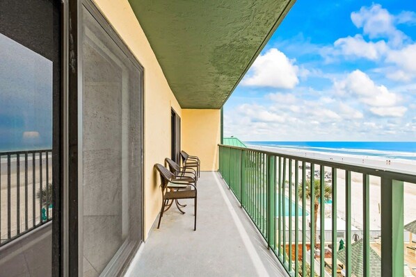 A balcony with a view of the beach, equipped with chairs and a railing.