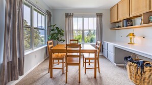 A dining area with a wooden table and chairs, large windows with curtains, a plant, and a wicker basket. - 28 Lodge 1 Bedroom Condo by RedAwning (Hood River)