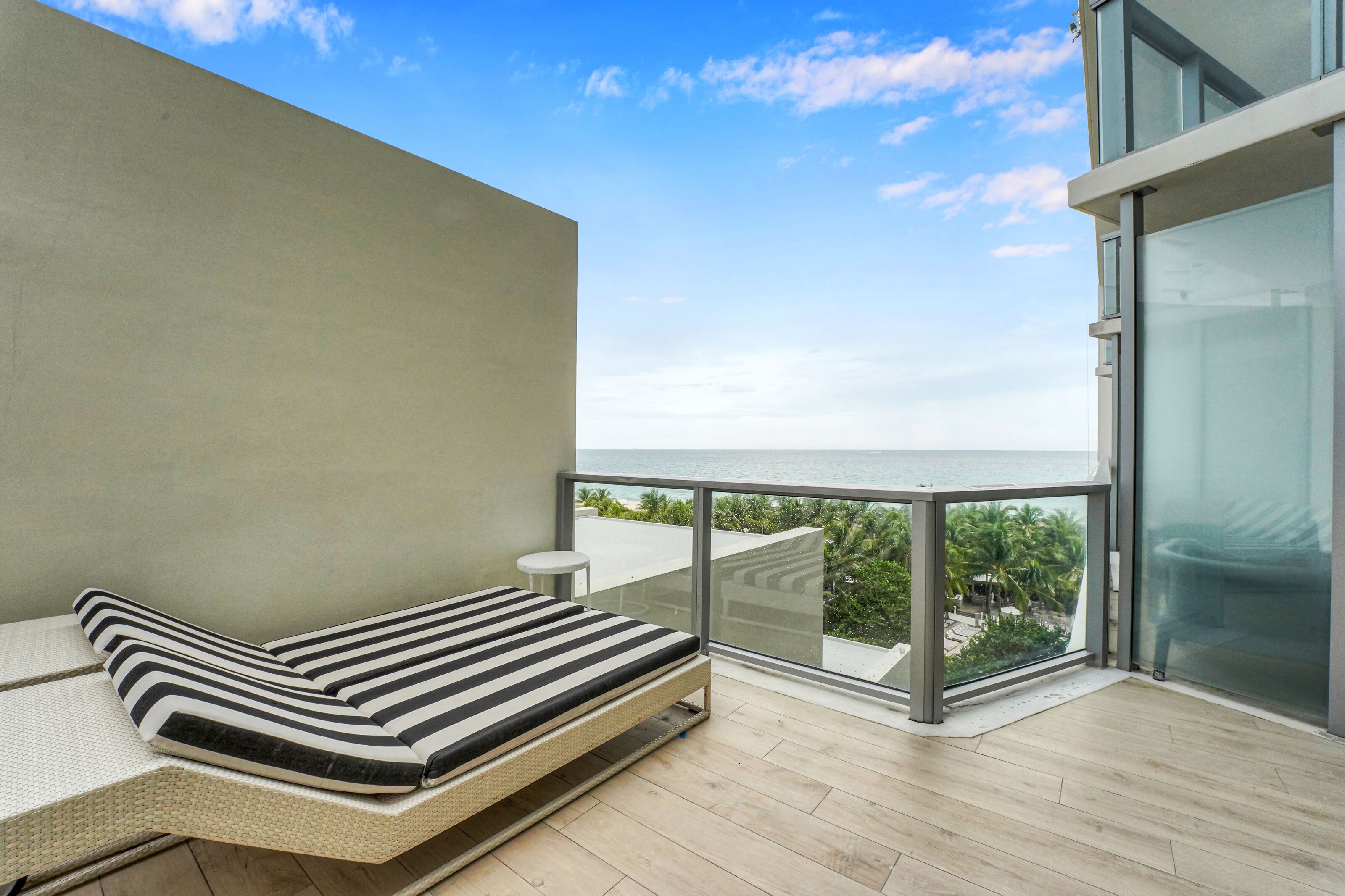 A balcony with a bed, a small table, and a glass railing overlooking a scenic view.