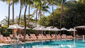 A pool area with lounge chairs and umbrellas, surrounded by palm trees.