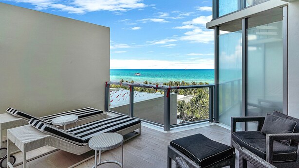 A balcony with a view of the ocean, a lounge area with striped chairs, and a wicker sofa.