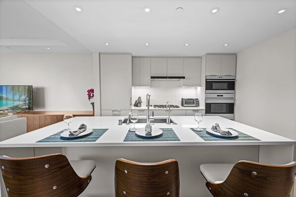 A modern kitchen with white cabinets, a central island with a sink, and a dining area with three wooden chairs.