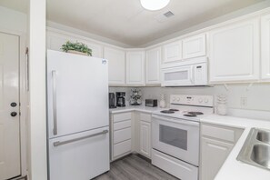 A kitchen with white cabinetry, a refrigerator, a microwave, a stove, and a sink.