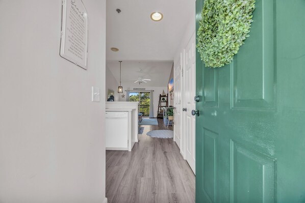 A hallway with a green door, white walls, and a ceiling fan.