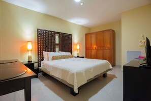A hotel room with a bed, bedside lamps, a wardrobe, a desk, and a television.