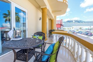 A balcony with a table and chairs, a view of a cruise ship, and a parking area.