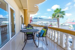 A balcony with a table and chairs, a view of a cruise ship, and a palm tree.