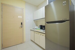 A compact kitchen with a stainless steel refrigerator, a wooden door, and a countertop with a kettle and a box of tissues.