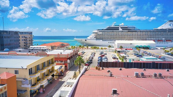 A cruise ship docked at a port with a view of the ocean and a cityscape in the background.