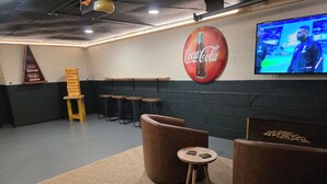 A room with a large Coca-Cola sign, a television, and several stools.