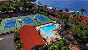 A tennis court complex with a pool and a view of the ocean.
