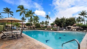 A swimming pool with lounge chairs and umbrellas, surrounded by palm trees and a clear sky.