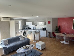 A modern kitchen with white cabinets, a dining area with a red wall, and a living room with a grey sofa.