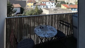 En balkong med utsikt över stadsbilden, ett runt bord med ett mönstrat bordsduksöverdrag och en bekväm sittplats.