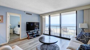 A modern living room with a flat-screen TV, a round coffee table, and a balcony with a view of the sea. - Breathtaking Ocean View, Beachfront Condo-Steps to Beach/Pools, Sea Colony East (Bethany Beach)