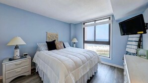 A bedroom with a bed, two bedside tables with lamps, a TV mounted on the wall, and a window with a view. - Breathtaking Ocean View, Beachfront Condo-Steps to Beach/Pools, Sea Colony East (Bethany Beach)