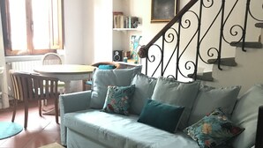 A living room with a light blue sofa, a patterned rug, a dining area with a table and chairs, and a staircase with a wrought iron railing. - Central Private home,  close to all you need in Viareggio (Viareggio)
