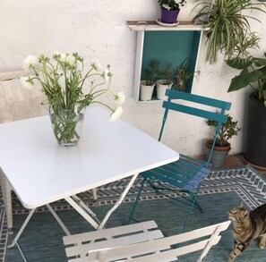 Ein weißer Tisch mit einer Glasvase voller Blumen, ein blauer Stuhl und ein gestreifter Boden.