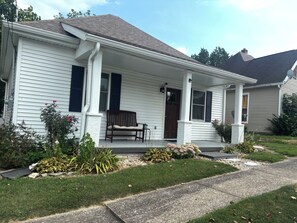 Une maison de plain-pied avec un porche à l’avant, un banc et un petit jardin.