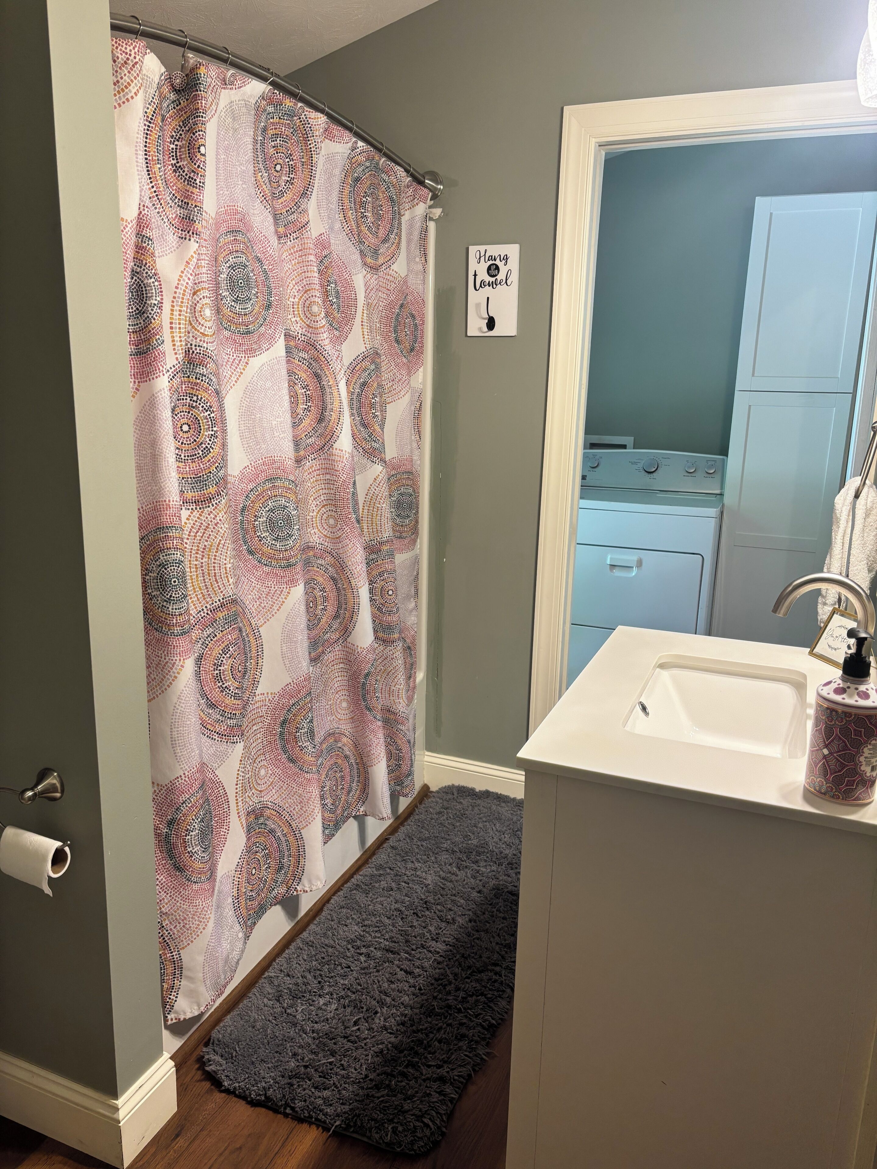 A bathroom with a shower curtain, a sink, a mirror, and a towel rack.