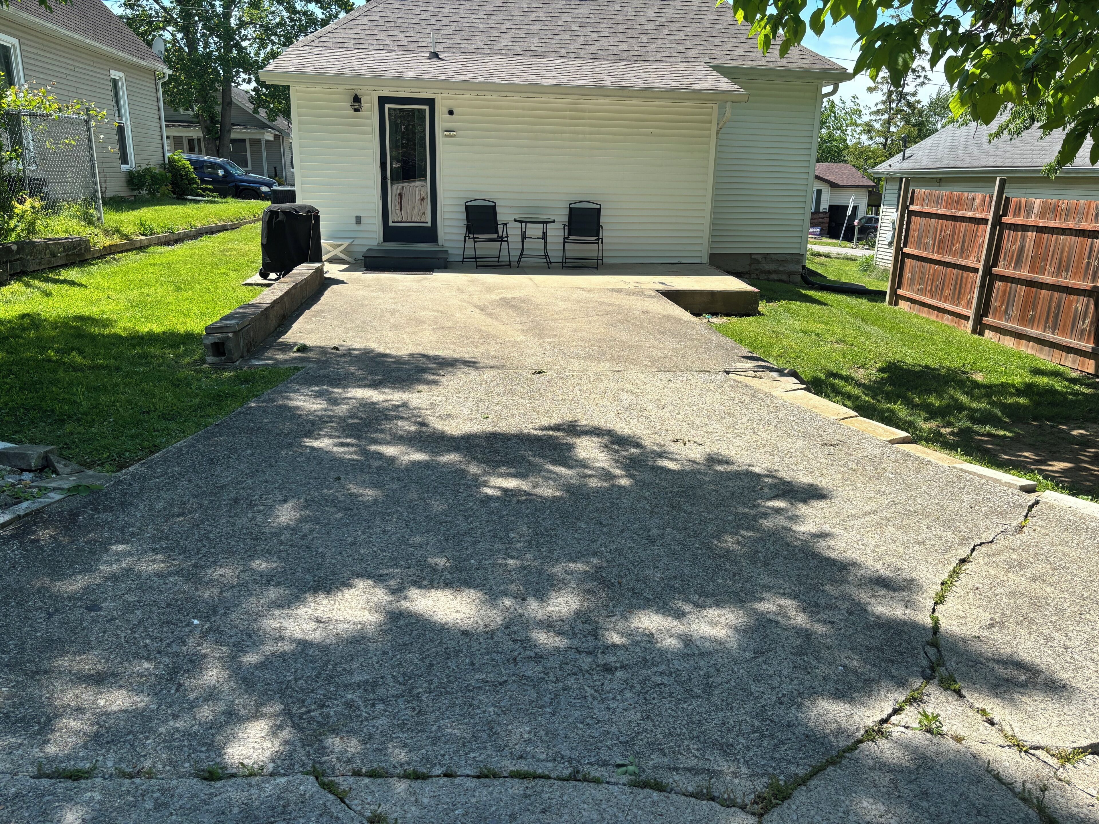 A residential property with a concrete driveway leading to a covered patio area with two chairs and a table.