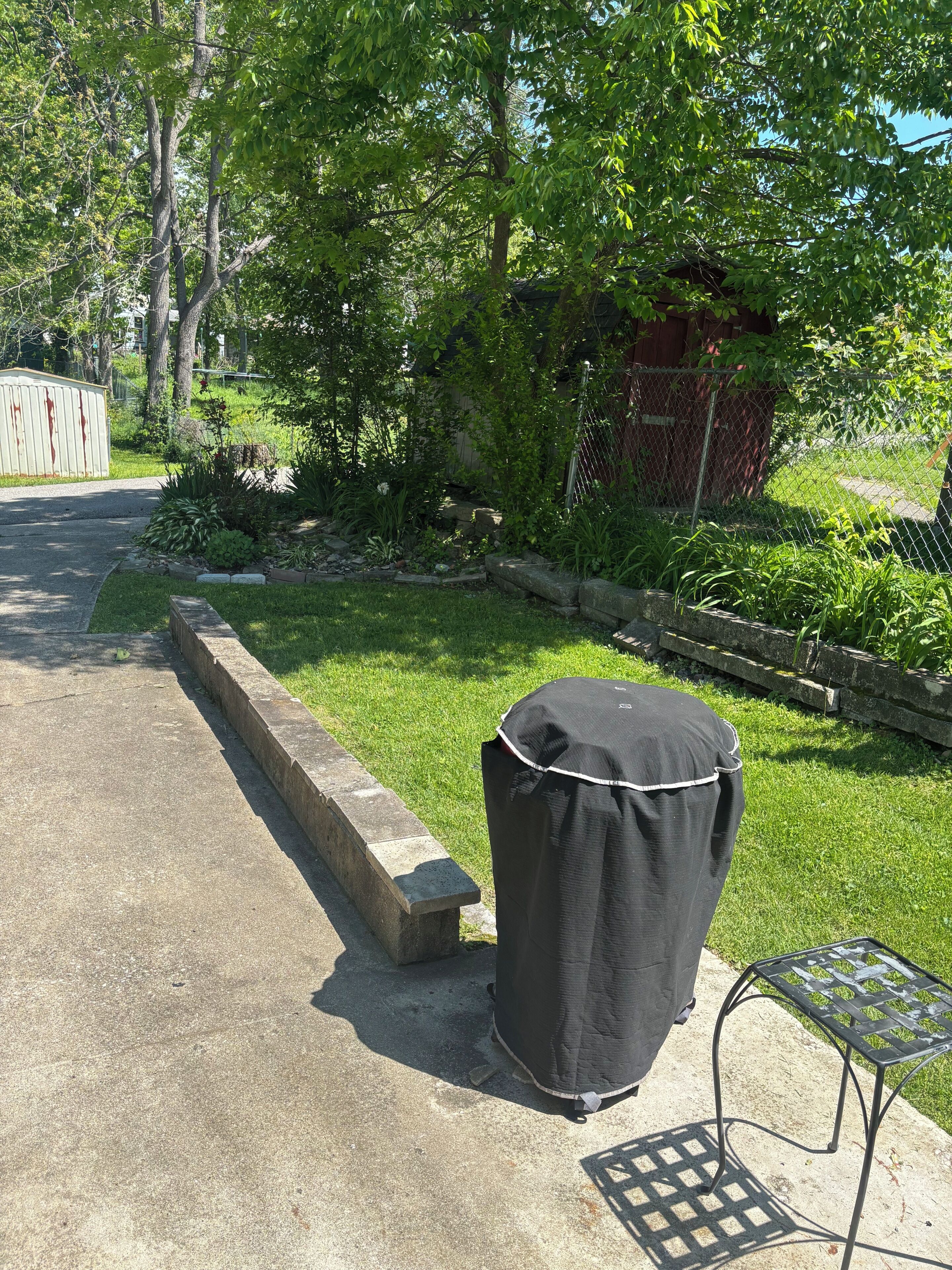 Un barbecue extérieur abrité, un bac à plantes en béton et une table en métal avec un plateau ajouré.