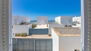 A view of a residential area with white buildings, a clear blue sky, and a calm sea in the background.