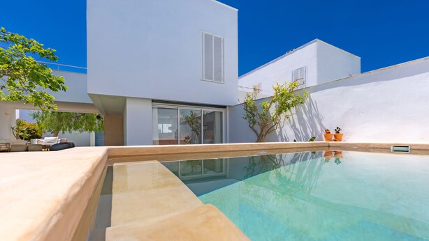 A modern outdoor swimming pool area with a clear blue pool, a white building with large windows, and a few potted plants.