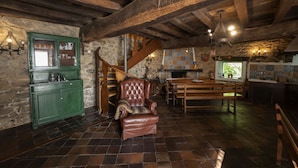 A rustic kitchen with exposed wooden beams, a green cabinet, a leather armchair, and a wooden dining table.