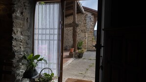 A stone building with a wooden door and a window with a curtain. There are potted plants and a basket on the windowsill.